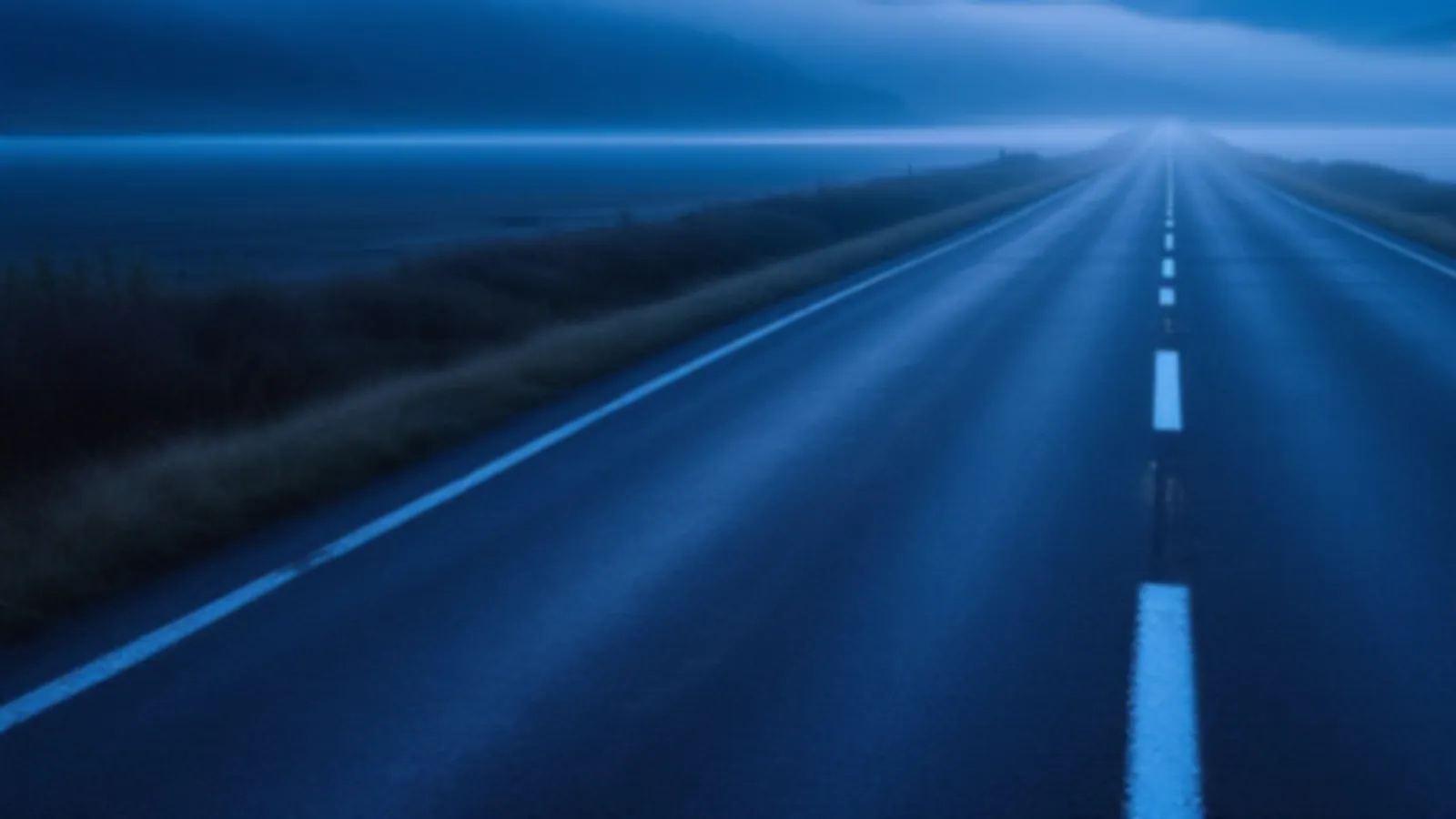 An empty lakeside road with soft mist on still water and blue hills beyond at dawn, the MilepostRate view of personal loan rates online, $100 – $5,000